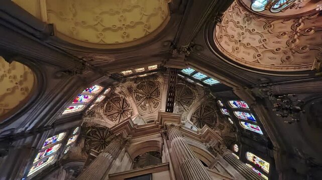 Historic Malaga cathedral interior featuring colorful stained glass windows, lavish carved ceiling decoration and towering stone columns, Spain