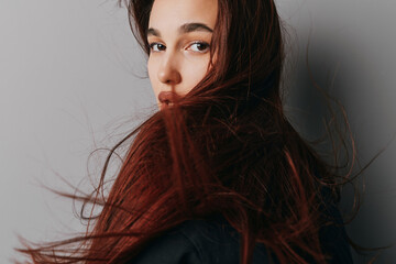 Young woman with long flowing hair looking over shoulder against plain background, natural makeup...