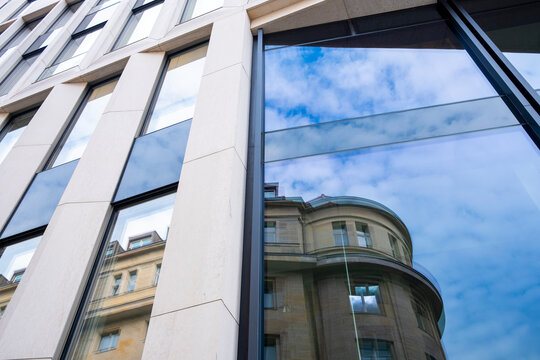 Modern office architecture glass facade with strong reflection of sky and urban surroundings showing contrast and angled perspective in daylight