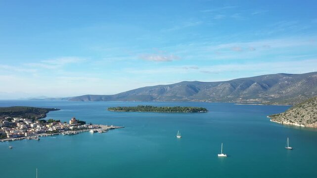 Scenic aerial view of Kilada bay with turquoise waters, sailboats, and a small island, surrounded by mountains in Greece.