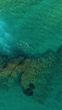 Drone shot of turquoise water and rocky shoreline in Acciaroli, Italy. The clear sea reveals underwater rocks and gentle waves.