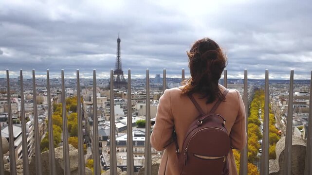 A tourist woman with a backpack on a sightseeing trip enjoys the panoramic view of the city of Paris, France