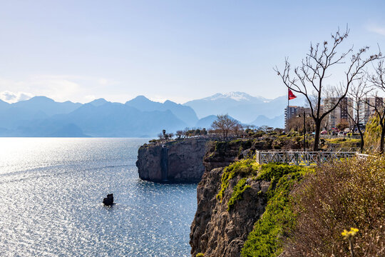 High angle view of Falez Park cliffs in Antalya. Bright sunlight reflects on the sea with mountains in a haze. Spring landscape with leafless trees and blue Mediterranean water in Turkey.