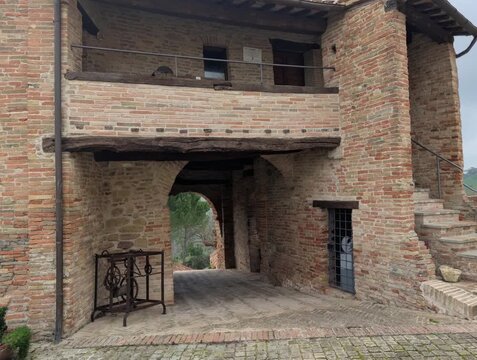 Edificio medievale in mattoni con arco e balcone, architettura storica italiana immersa nel verde