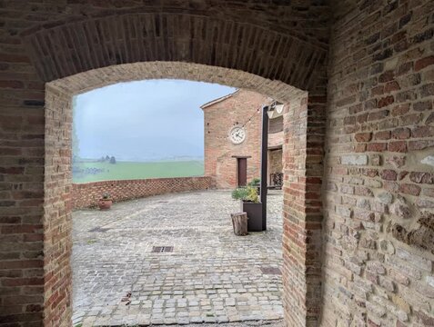 Cortile storico in mattoni visto attraverso un arco, atmosfera medievale italiana tra architettura antica e paesaggio verde