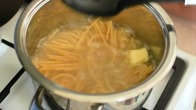 Spaghetti submerged in boiling water inside cooking pot. Spaghetti moves gently during boil, steam fills kitchenaid, pasta preparation moment, home cooking routine concept