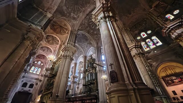 Historic Malaga cathedral interior featuring colorful stained glass windows, lavish carved ceiling decoration and towering stone columns, Spain
