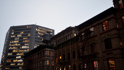 An old historic building stands beside a tall glass skyscraper as dusk falls over the city. The warm lights from the windows add charm to the evening atmosphere. © icetray