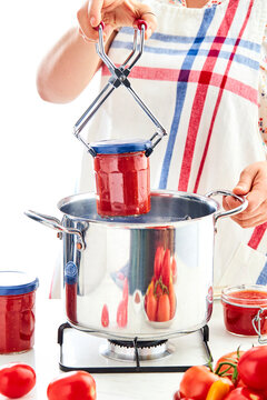 woman hands placing a jar of tomato sauce into a pot of boiling water in a kitchen setting