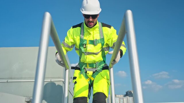 Young man engineer climbing a metal ladder to inspect industrial equipment, emphasizing safety standards and maintenance operations