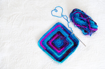 Crochet square being created with blue and purple yarn on a white surface in daylight