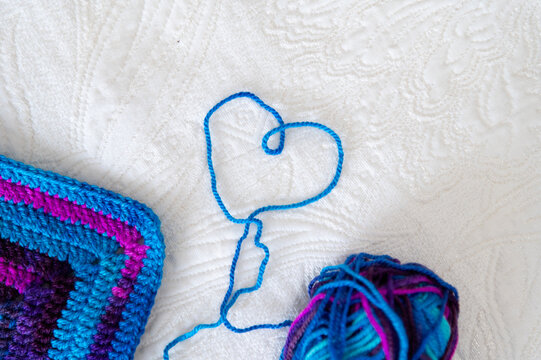 Crochet project with blue yarn making heart shape on white fabric