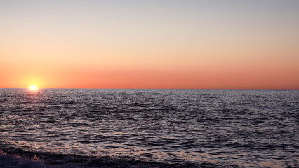 Obraz premium Sunset over calm ocean waters with colorful sky and gentle waves