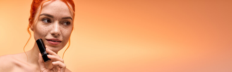 Stylish young woman applying lipstick against a warm orange backdrop