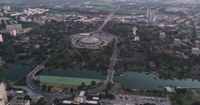 Aerial view of the Palazzo dello Sport and surrounding green spaces, bisected by a lake with bridges in the sprawling urban landscape, Rome, Lazio, Italy.