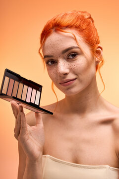 Stylish young woman showcasing a stunning makeup palette with vibrant backdrop