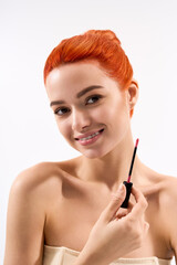 Fototapeta premium Stylish young woman applies lipstick with a confident smile in a bright setting