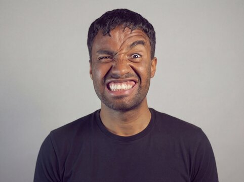Man making a funny, angry face, gritting teeth, eyes squinting, showing intense emotion and a stressed expression