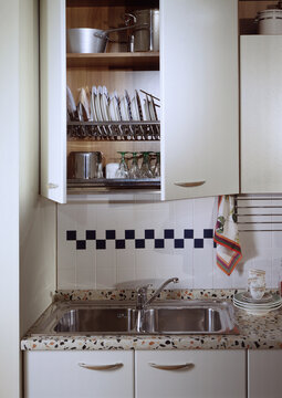 Close up of a kitchen cabinet with a steel sink and a dish drainer wall unit