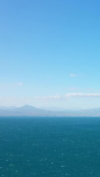 Wide view of a calm blue sea with distant mountains under a clear sky, likely near Corinth, Greece. Ideal for concepts of tranquility and natural beauty.