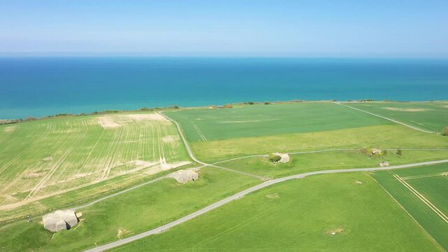 Drone shot of green fields and historic bunkers overlooking the blue sea at Batterie de Longues sur Mer, Normandy, France.