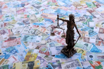 Themis figure against the background of pile of different currencies money bills. Concept of justice and corruption around the world