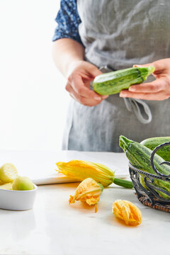 Zucchinis and zucchini blossoms in a kitchen setting with a female figure in the background