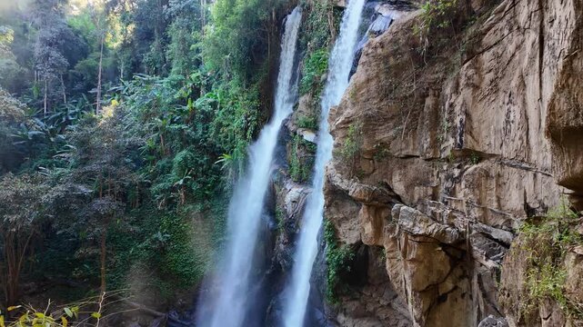 Capture the natural beauty of Mok Fa Waterfall in Chiang Mai. Lush greenery surrounds the cascading water, creating a serene and vibrant scene. Ideal for tranquil nature projects.