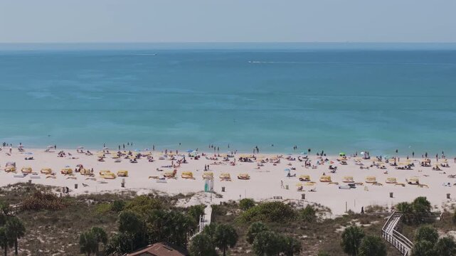 Aerial view of Gulf of Mexico from Saint Pete Beach showing white sand, turquoise waters, beachgoers with colorful umbrellas, and parasailing in Florida's premier beach destination.