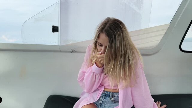 Young blonde woman feeling seasick on a motor boat, covering her mouth with hand due to nausea. Concept of motion sickness, travel discomfort, sea travel and marine transportation