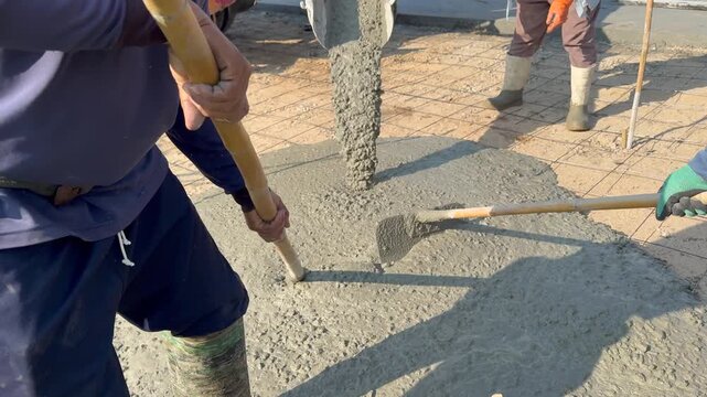 Workers Spreading Wet Concrete Over Reinforcement Steel Grid During Foundation Pour