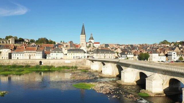 Scenic view of the historic stone bridge and charming old town of La Charite sur Loire under a clear blue sky. Picturesque French architecture lines the riverbank.