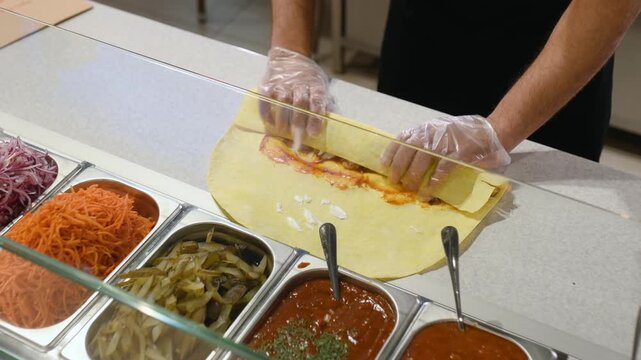 A fast food chef makes a kebab by putting sauce, chicken, vegetables, and other ingredients on pita bread.