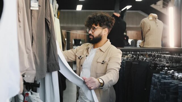 Man inspects clothing items on racks in a retail store, featuring a variety of beige and light-colored garments in an organized display