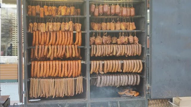 Wędzarnia z wiszącymi wędlinami i kiełbasami, tradycyjne wędzenie mięsa w komorze, rzędy wyrob&oacute;w na hakach.