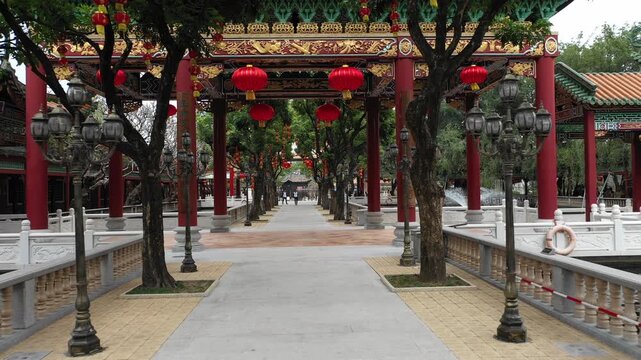 Low angle drone shot through trees filled with red lanterns in temple complex of classic Chinese garden in Guangzhou
