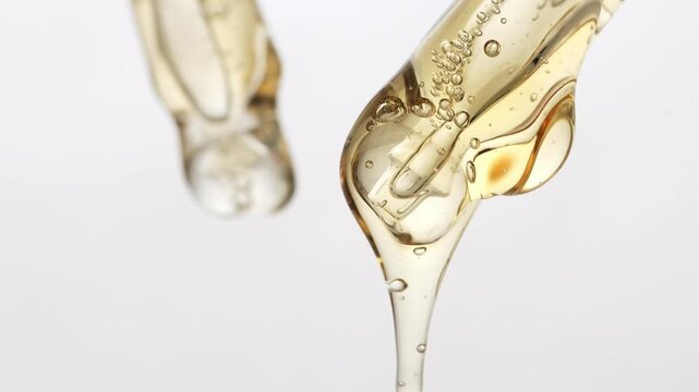 Facial serum, shampoo gel slowly flows from the pipette and drips, macro, neutral background.