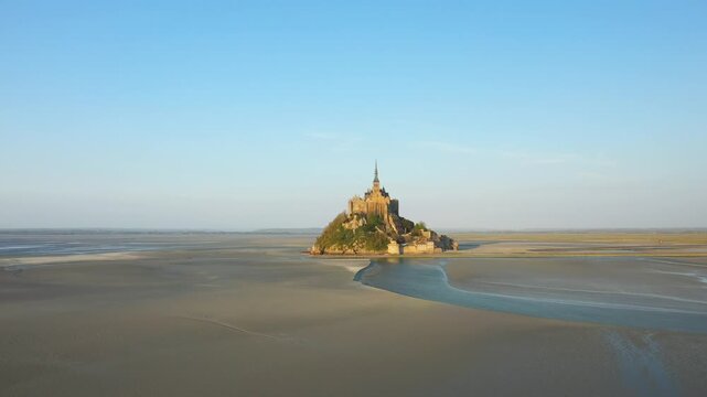 Aerial view of Mont Saint Michel island surrounded by tidal flats under a clear blue sky in Normandy, France.