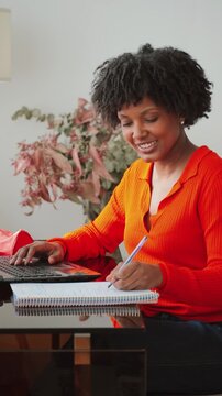 A focused woman engaged in creative writing is using a laptop while taking notes in a notebook, demonstrating productivity and concentration in her work, showcasing determination and motivation.