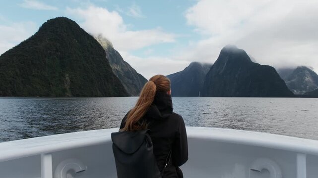 Traveler on boat cruising through Milford Sound fjord surrounded by dramatic mountains, Fiordland National Park, New Zealand