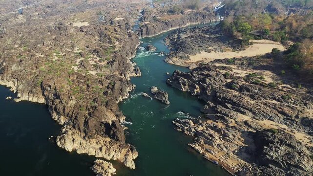 Aerial view of the rocky river landscape at Li Phi Falls, also known as Tat Somphamit Waterfalls, during sunrise in Laos. Rugged rocks and sparse vegetation line the winding river.