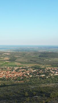 Scenic aerial landscape of Opoul Perillos in southern France, featuring patchwork fields, a small village, and the Mediterranean Sea under a clear blue sky.