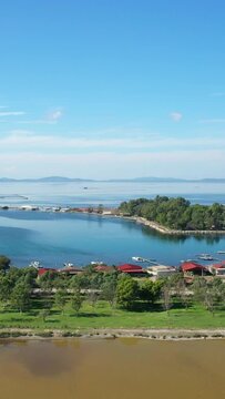 Aerial view of the picturesque village and lagoon landscape of Tourlida, with traditional houses, calm waters, and distant mountains under a clear blue sky in Greece.