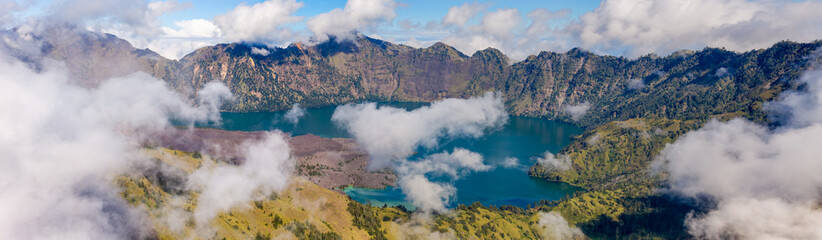 Wide panoramic view of a stunning volcanic crater lake partially hidden by white clouds