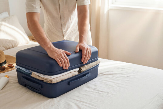 Man closing packed suitcase on bed, preparing for summer vacation with copy space
