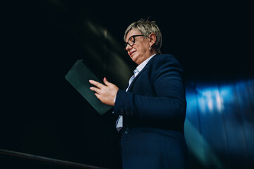 Senior businesswoman smiling while using stylus on tablet, representing joy, confidence, and professional engagement with mobile digital tools in modern work culture.