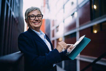 Portrait of smiling mature woman using stylus on digital tablet, expressing satisfaction and...