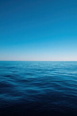 Obraz premium Calm deep blue ocean horizon under clear sky with smooth gentle waves and minimal seascape, tranquil open water conveying serene reflection and infinite expanse