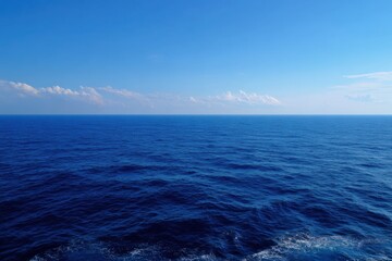Fototapeta premium Deep calm blue ocean horizon under soft clouds with gentle swells and sparkling surface on a bright day