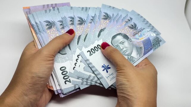 Person hands holding stack of Indonesian Rupiah banknotes on white background